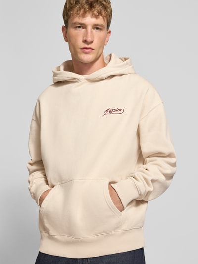 Männermodel trägt Regular Fit Hoodie aus Baumwoll-Mix von PEGADOR in Beige mit Kängurutasche, Strass-Logo, Nahaufnahme Oberkörper.