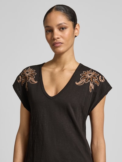Frauenmodel trägt T-Shirt aus reiner Baumwolle von Scotch & Soda in Schwarz mit floralen Stickereien, taillierte Passform, Nahaufnahme Oberkörper.