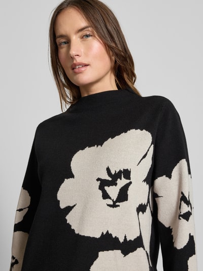Frauenmodel trägt Strickpullover mit geripptem Stehkragen von Betty Barclay, Viskose-Mix, schwarzer Stoff mit beigefarbenem Blumenmuster, Nahaufnahme Oberkörper.