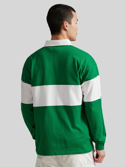Männermodel trägt Regular Fit Poloshirt aus reiner Baumwolle von Polo Ralph Lauren in Grün mit breitem weißen Streifen, Piqué-Struktur, Ganzkörperansicht Rückansicht.