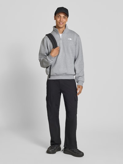 Mannenmodel draagt Regular Fit Sweatshirt met Troyer Model "EVOLUTION" van The North Face in grijs katoenmix, met gestikt logo, elastische boorden, ruglengte maat M 67 cm, mouwlengte maat M 68 cm, full body voorkant.