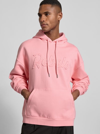 Männermodel trägt Hoodie mit Statement-Stitching von Dsquared2 in Rosa, reine Baumwolle, Relaxed Fit, Känguru-Tasche, Nahaufnahme Oberkörper.