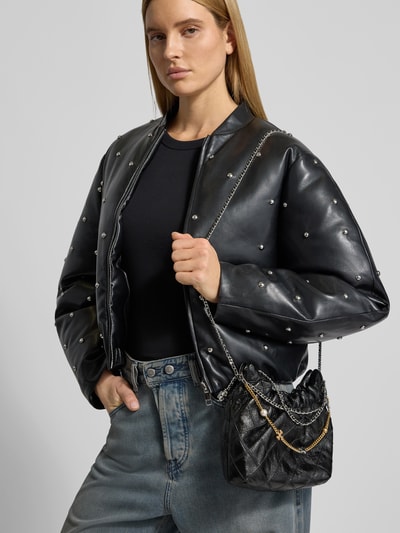 Frauenmodel trägt Shoulder Bag in Leder-Optik von Tory Burch mit Zierkette, Strukturmuster, Ketten-Optik und offenem Hauptfach, Nahaufnahme Oberkörper.