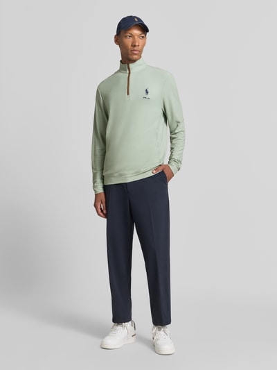 Männermodel trägt Regular Fit Troyer mit kurzem Reißverschluss von Polo Ralph Lauren in lichtgroen met ritssluiting, donkere broek, lichte sneakers, Ganzkörperansicht von vorne.