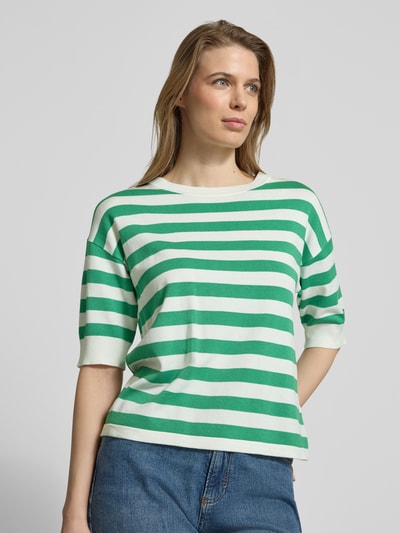 Modelka kobieca nosi zielono-biały damski t-shirt w paski z mieszanki wiskozy, krój regular fit, model 'Morla' od b.young, okrągły dekolt, rękaw o dł. 7/8, długość tyłu w rozmiarze S: 57 cm, długość rękawów: 23 cm, widok na górną część ciała z przodu.
