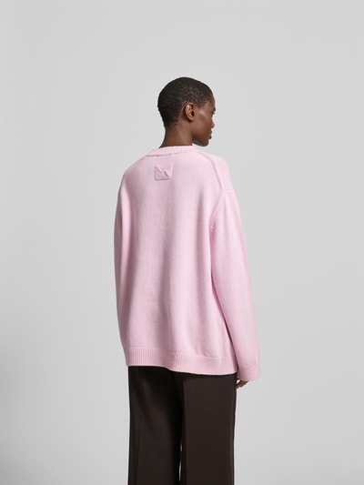 Frauenmodel trägt Oversized Wollpullover aus Woll-Mix von Nanushka in Hellrosa mit Strick-Optik und gerippten Abschlüssen, Rückenansicht.