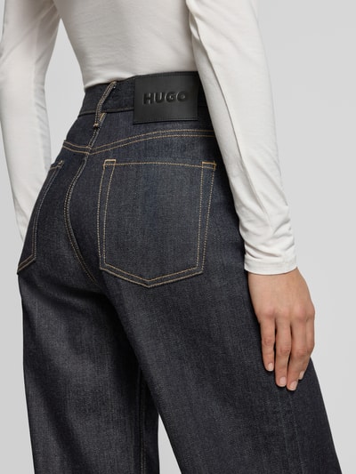 Frauenmodel trägt Wide Leg Jeans aus Baumwoll-Mix Modell 'GEABENA' von HUGO in Melange-Optik mit Label-Patch, Nieten, Kontrastnähten, 5-Pocket-Design, Denimstruktur, Detailaufnahme Rückansicht.