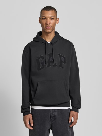Mannelijk model draagt Hoodie met Logo-Detail en Känguru-Tasche van GAP in zwart, katoenmix, loose fit, met capuchon en zak, geribde boorden, volledige vooraanzicht bovenlichaam.