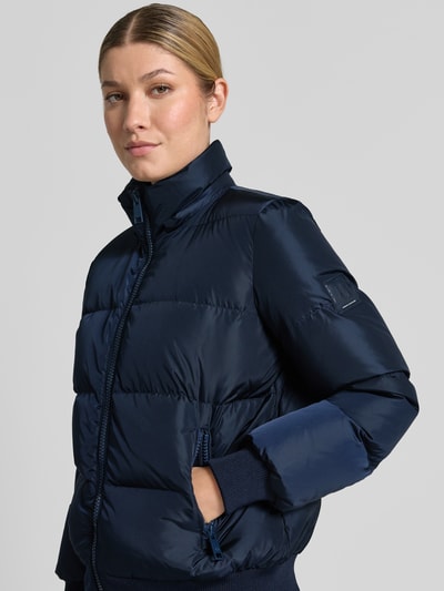 Frauenmodel trägt Steppjacke mit Daunen-Feder-Füllung von Armani Exchange in Dunkelblau, glänzende Oberfläche, Regular Fit, Nahaufnahme Oberkörper. Rückenlänge 60 cm, Brustweite 50 cm, Schulterbreite 41 cm, Ärmellänge 62 cm, elastischer Mix, Stehkragen, Zweiwege-Reißverschluss, Reißverschlusstaschen, Kapuze.