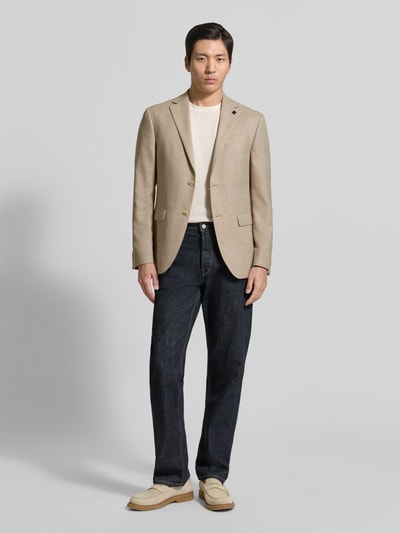 Męski model nosi Regular Fit Blazer mit Viskose-Anteil od HECHTER PARIS, beżowy, elastyczna mieszanka materiałów, aplikacja z logo, brustasza, kieszenie z wypustkami, listwa z 2 guzikami, kołnierz z połami, długość tyłu w rozmiarze 50: 72 cm, szerokość ramion w rozmiarze 50: 38 cm, długość rękawów w rozmiarze 50: 64 cm, Ganzkörperansicht von vorne.