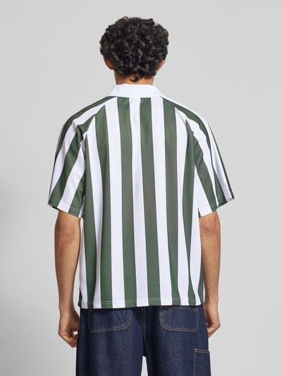 Männermodel trägt grün-weiß gestreiftes Loose Fit Poloshirt mit Motiv-Print Modell 'ZIDAN' von Only & Sons, Piqué, Ganzkörperansicht Rückansicht.