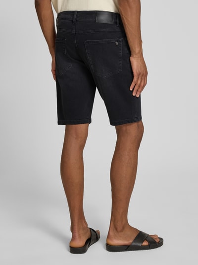 Männermodel trägt Regular Fit Jeansshorts aus Baumwoll-Mix Modell 'RE.MAINE SHORTS BO BORN' von BOSS Orange in Denim-Optik mit Label-Patch, Nieten, Gürtelschlaufen und 5-Pocket-Design, Ganzkörperansicht Rückansicht.
