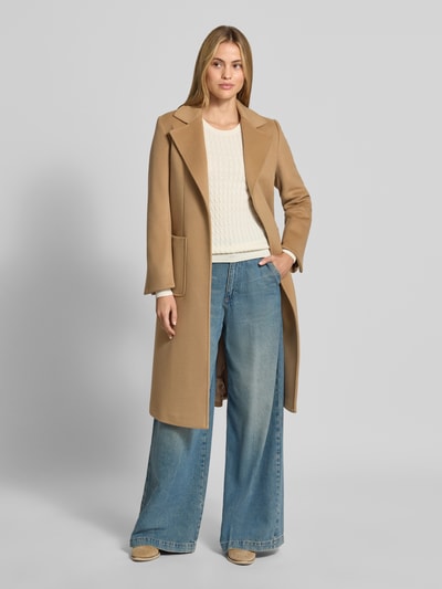 Frauenmodel trägt Slim Fit Strickpullover mit Zopfmuster von Christian Berg Woman in Creme, Baumwoll-Mix, Rundhalsausschnitt, langärmlig, gerippte Blende, kombiniert mit beigem Mantel und weiter Jeanshose, Ganzkörperansicht von vorne.