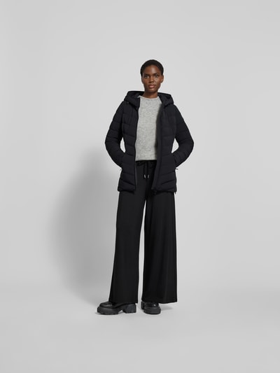 Frauenmodel trägt schwarze Daunenjacke mit Kapuze von Moose Knuckles, Material-Mix mit Stretch-Anteil, taillierter Schnitt, Ganzkörperansicht von vorne.