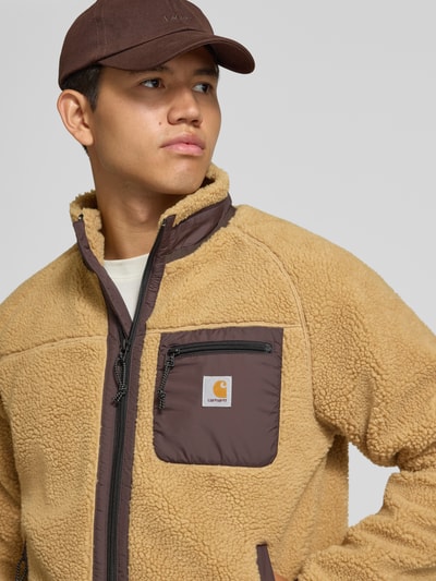 Männermodel trägt Teddyjacke mit Brusttasche Modell 'PRENTIS LINER' von Carhartt Work In Progress, beige und braun, Nahaufnahme Oberkörper. Herren Teddyjacke Regular Fit, Stehkragen, Reißverschlüsse, Label-Patch, Kontext: Rückenlänge 65 cm, Ärmellänge 51 cm.