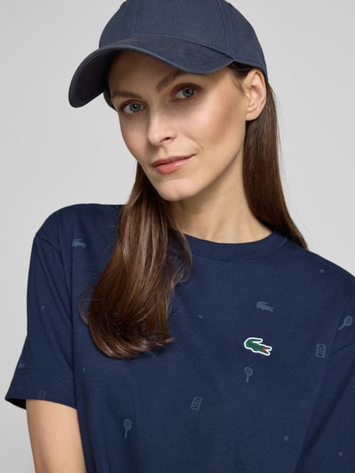 Frauenmodel trägt Oversized T-Shirt aus Baumwoll-Mix von Lacoste Sport in Dunkelblau mit Tennis-Print und Logo-Patch, Nahaufnahme Oberkörper.