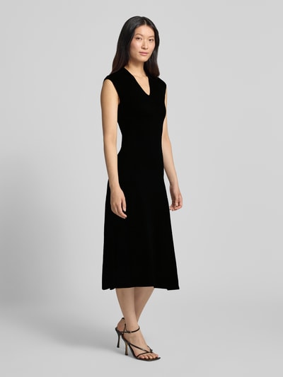 Frauenmodel trägt Kleid aus Viskose-Mix Modell 'CANELONS' von MANGO in Schwarz, taillierte Passform, V-Ausschnitt, Midilänge, Ganzkörperansicht von vorne.