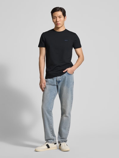 Männermodel trägt T-Shirt mit Label-Detail van Gant in zwart, recht model, ronde hals, puur katoen, ruglengte maat M 70 cm, geheellichaamsvooraanzicht.