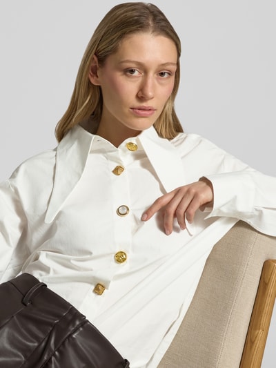 Frauenmodel trägt Oversized Hemdbluse aus reiner Baumwolle Modell 'JOMATO' von Essentiel Antwerp in Unifarbe Weiß, spitzer Kragen, goldfarbene Knöpfe, Nahaufnahme Oberkörper.