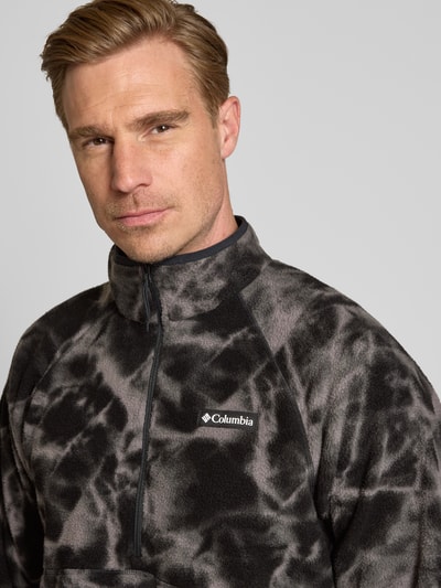 Männermodel trägt Fleecepullover mit Label-Details Modell 'Timber Crest™' von Columbia, grau-schwarze Muster, Nahaufnahme Oberkörper. Rückenlänge 70 cm, Ärmellänge 73 cm, gerader Schnitt, Stehkragen, Reißverschluss.