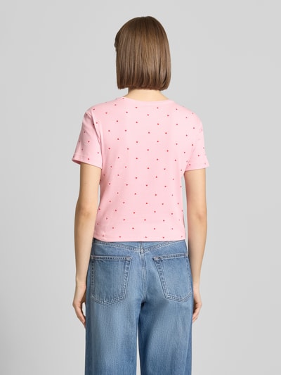 Frauenmodel trägt Regular Fit T-Shirt aus Baumwoll-Mix Modell 'FENJA' von Only, Optik: Allover-Muster, Motiv-Print, Kurzarm, Rundhals, Feinripp, Rosa mit kleinen roten Punkten, glatte Struktur, Ganzkörperansicht Rückansicht.