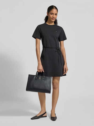 Frauenmodel trägt Henkeltasche in Leder-Optik von Tommy Hilfiger, Optik: unifarben, Magnetverschluss, Logo-Applikation aus Metall, Tragehenkel, Ganzkörperansicht von vorne.
