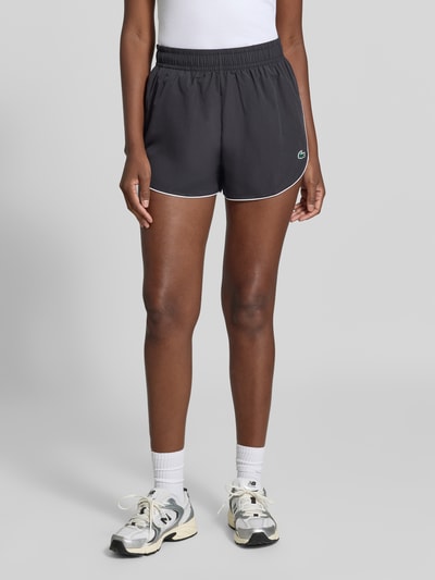 Frauenmodel trägt schwarze Regular Fit Sportshorts mit elastischem Bund von Lacoste, Damen Sportshorts, Nahaufnahme Unterkörper.