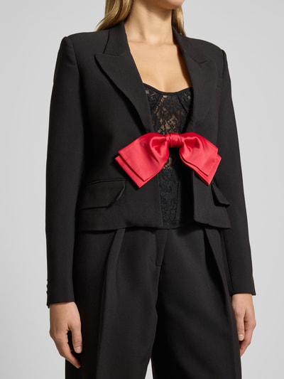 Frauenmodel trägt Blazer mit Reverskragen Modell 'DILONE' von Bardot, Material-Mix mit Viskose-Anteil, Regular-Fit, Schleifen-Detail, Pattentaschen, schwarze Farbe mit rotem Schleifen-Detail, Rückenlänge bei Größe 36: 53 cm, Nahaufnahme Oberkörper.