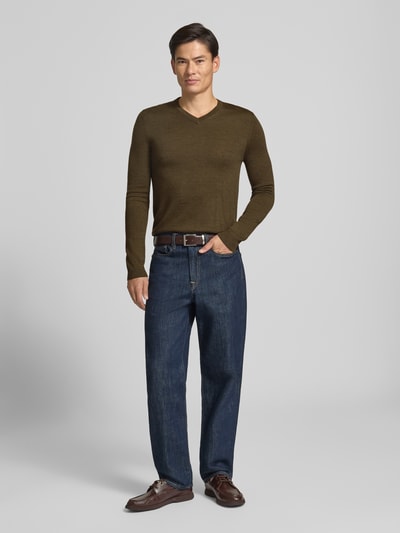 Männermodel trägt Strickpullover aus Woll-Mix mit V-Ausschnitt von Christian Berg Men in Oliv, dunkle Jeans, neutraler Hintergrund, Ganzkörperansicht von vorne. Regular Fit, gerippte Abschlüsse, Rückenlänge 71 cm, Ärmellänge 73 cm.