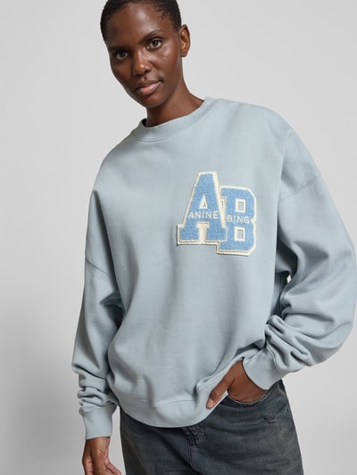 Frauenmodel trägt Oversized Sweatshirt aus reiner Baumwolle von Anine Bing in Hellblau mit Label-Detail, elastische Abschlüsse, Rundhalsausschnitt, Rückenlänge 64 cm bei Größe S, Ganzkörperansicht von vorne.