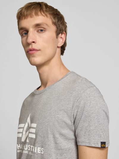 Männermodel trägt T-Shirt mit Logo und Rundhalsausschnitt von Alpha Industries aus Reine Baumwolle, Regular-Fit, graue Farbe, Nahaufnahme Oberkörper.