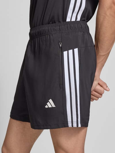 Männermodel trägt Shorts mit Logo-Print und Reißverschlusstaschen von adidas Training, Schwarz mit weißen Streifen, Lockerer-Schnitt, Elastischer-Bund, Seitliche-Reißverschlusstaschen, Bundweite 38 cm, Innenbeinlänge 14 cm, Nahaufnahme Oberkörper.