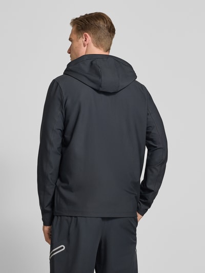 Männermodel trägt Regular Fit Jacke mit Logo-Print Modell 'Unstoppable' von Under Armour in dunklem Ton, elastischer Material-Mix, Kapuze, Rückansicht Ganzkörperansicht. Rückenlänge Größe M 74 cm, Reißverschlusstaschen, sportlicher Look.