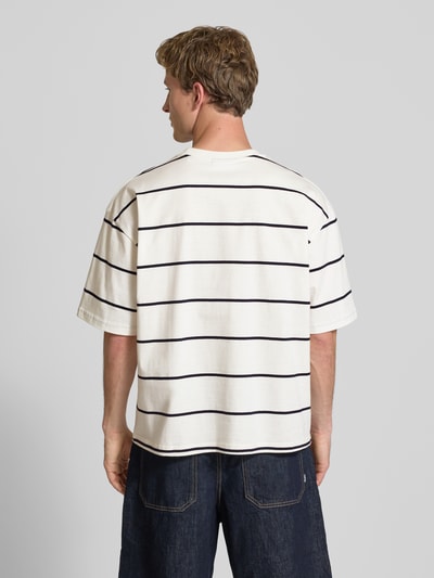 Männermodel trägt T-Shirt mit Rundhalsausschnitt und Logo-Stitching von REVIEW, weiße Baumwolle, schwarze Streifen, Loose Fit, Rückenlänge 67 cm, Ganzkörperansicht Rückansicht.