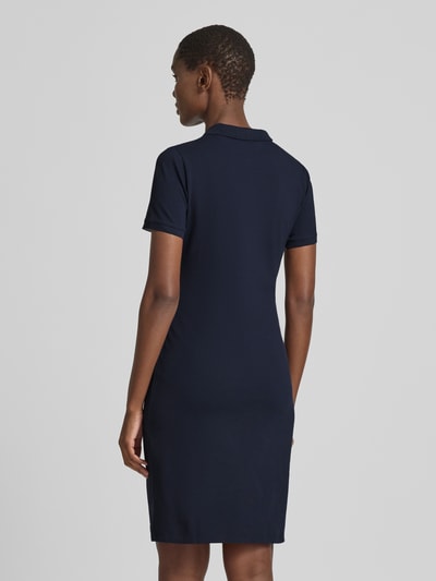 Frauenmodel trägt knielanges Polokleid mit Label-Stitching von Gant in Dunkelblau, gerader Schnitt, Rückansicht Ganzkörperansicht. Baumwoll-Elasthan-Mix, Knopfleiste, kurze Ärmel, dezentes Texturfinish.