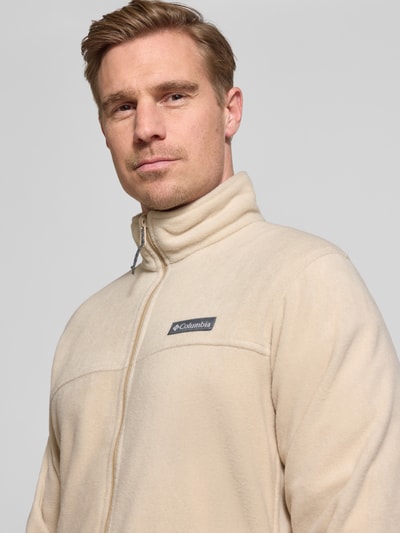 Männermodel trägt Regular Fit Fleecejacke mit Logo-Patch Modell 'Mountain' von Columbia in Beige mit Stehkragen und Reißverschluss, Nahaufnahme Oberkörper.