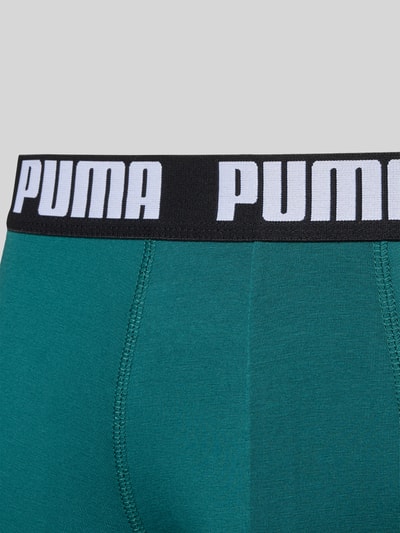 Mężczyzna nosi Trunks aus Baumwoll-Mix im 2er-Pack od PUMA w kolorze zielonym z czarną elastyczną gumką i logo, zbliżenie na talię, dopasowany krój, bawełna z elastanem, detal z logo na pasku, 2 sztuki w opakowaniu.
