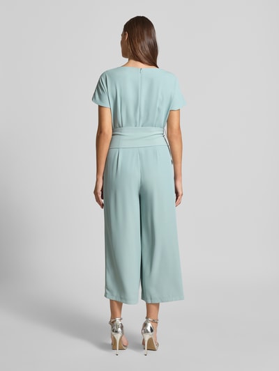 Frauenmodel trägt Jumpsuit mit Stretch-Anteil von Betty Barclay in Hellblau, Elastischer-Material-Mix, Regular-Fit, Kurzärmelig, 7/8-Länge, Gelegte Falten, Gürtel auf Taillenhöhe, Ganzkörperansicht Rückansicht.