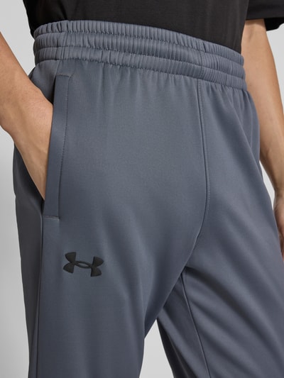 Męski model nosi Sweatpants mit elastischem Bund od Under Armour, luźny krój, elastyczny pas, kieszenie boczne, zbliżenie na biodra.
