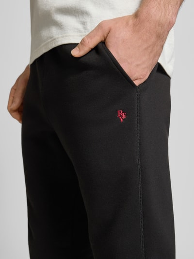 Männermodel trägt Sweatpants mit elastischem Bund von REVIEW aus Baumwoll-Mix, Slim Fit, schwarzes Material mit rotem Logo, Nahaufnahme Oberkörper.