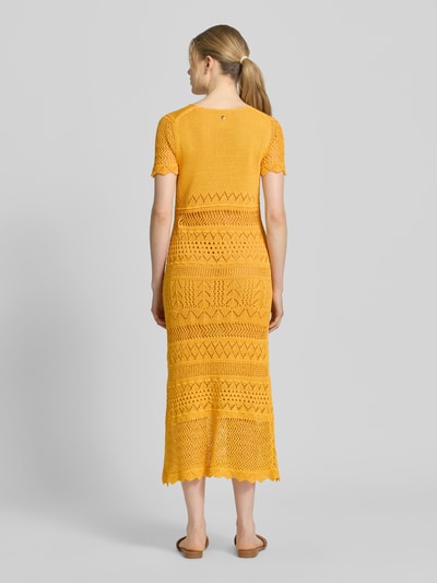 Frauenmodel trägt Strickkleid aus Baumwolle in Midilänge von Marc Cain in Gelb, Lochmuster, Muschelsaum, eng anliegende Passform, kurzärmelig, Rückenlänge 123 cm, Brustweite 39 cm, Ärmellänge 20 cm, Ganzkörperansicht Rückansicht.
