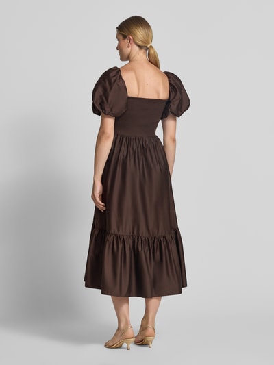 Frauenmodel trägt Cocktailkleid mit Smok-Details und Puffärmeln von Jake*s Cocktail, braun, A-Linie, reine Baumwolle, Ganzkörperansicht Rückansicht.