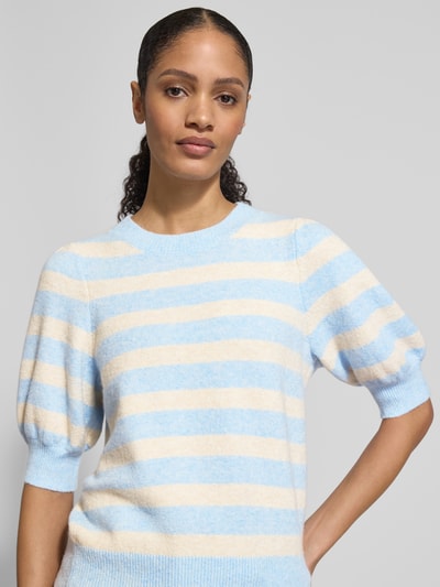 Frauenmodel trägt Regular Fit Strickpullover mit Crew Neck Modell 'DOFFY' von Vero Moda, Optik: Unifarben, Strickoptik, Label-Stitching-Applikation, Rundhals, 1/2-Arm, gerippte Abschlüsse, Materialverarbeitung: Strick, sanfte Blau-Beige-Streifen, weiche Textur, Ganzkörperansicht von vorne.