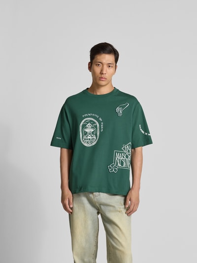 Männermodel trägt Oversized T-Shirt aus Bio-Baumwolle von MAISON KITSUNÉ, dunkelgrün mit weißem Label-Print, gerippter Rundhalsausschnitt, kurzärmelig, Rückenlänge bei Größe M 71 cm, Ganzkörperansicht von vorne.