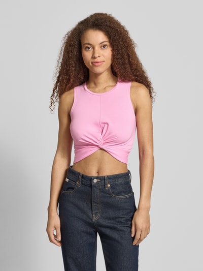 Modelka kobieca nosi Crop Top mit Knotendetail Modell 'TWIGGI' od Noisy May, różowy kolor, bawełniany miks ze stretchem, przód z węzłem, okrągły dekolt, długość tyłu w rozmiarze S: 37 cm, cała sylwetka z przodu.