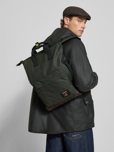 Männermodel trägt olivgrünen Rucksack mit labelpatch Modell 'FIELD WAX' von Barbour, Heren rugzakfunctie, Ganzkörperansicht Rückansicht