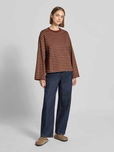 Kobiece modelka nosi bluzkę z długim rękawem 'Relaxed Fit Langarmshirt aus reiner Baumwolle' od Gina Tricot, brązowe paski, krój relaxed fit, okrągły dekolt, bawełna, długość tyłu w rozmiarze S: 62 cm, widok całej sylwetki z przodu.