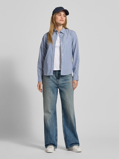 Frauenmodel trägt Regular Fit Bluse mit Label-Stitching von Gant, gestreiftes Hellblau, reine Baumwolle, Hemdblusenkragen, Ganzkörperansicht von vorne.