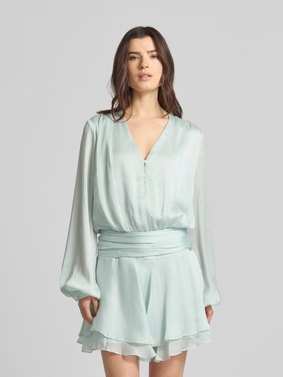 Frauenmodel trägt Minikleid mit kurzer Knopfleiste Modell 'MAGALI' von Guess in Hellblau, Taillierter Schnitt, V-Ausschnitt, Volantsaum, Ganzkörperansicht von vorne.
