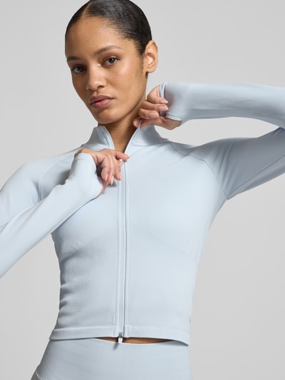 Modelka kobieca nosi Jacke mit Stehkragen und Zweiwege-Reißverschluss od aim'n, mieszanka materiałowa ze stretchu, krój slim fit, stójka, długość tyłu w rozmiarze S: 42 cm, szerokość ramion w rozmiarze S: 42 cm, szerokość w biuście w rozmiarze S: 38 cm, długość rękawa w rozmiarze S: 52 cm, jasnoniebieski kolor, gładka tekstura, zbliżenie na górną część ciała